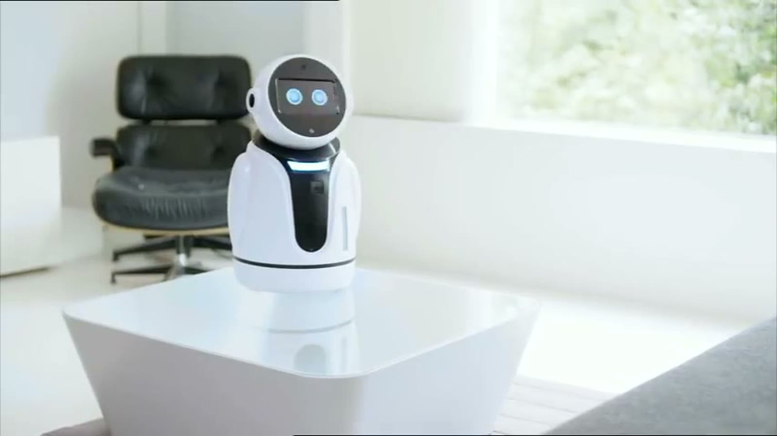 Jess, a small white robot with a round head, on a coffee table in a bright living room