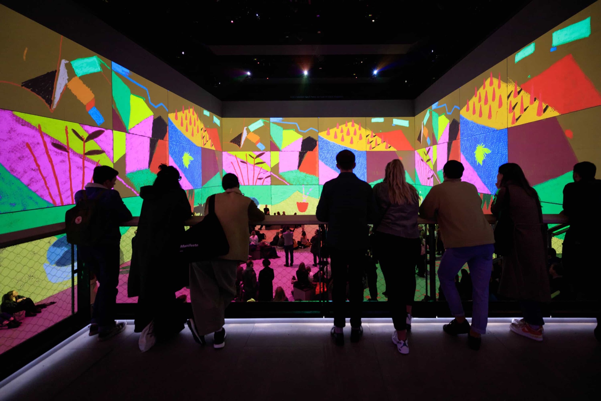 Visitors on a balcony at Lightroom, silhouetted against an iPad painting of bold pink, yellow and blue shapes that wraps around the whole room