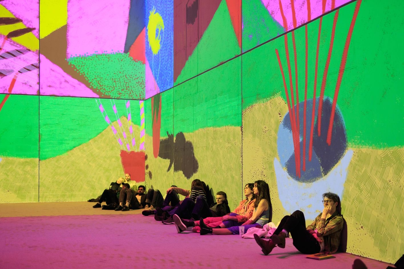 Visitors sitting against a wall at Lightroom, surrounded by one of Hockney&rsquo;s iPad paintings projected across the walls and floor
