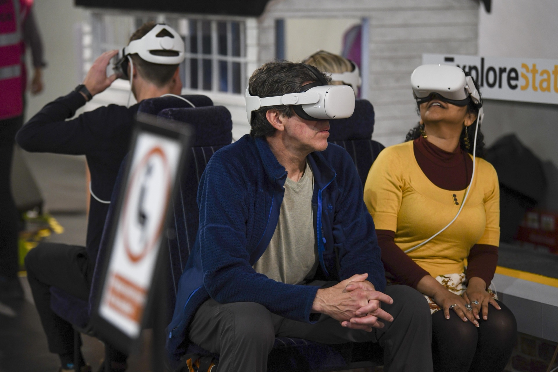 Three visitors in VR headsets sitting in real train seats beneath an ExploreStation sign at the National Railway Museum