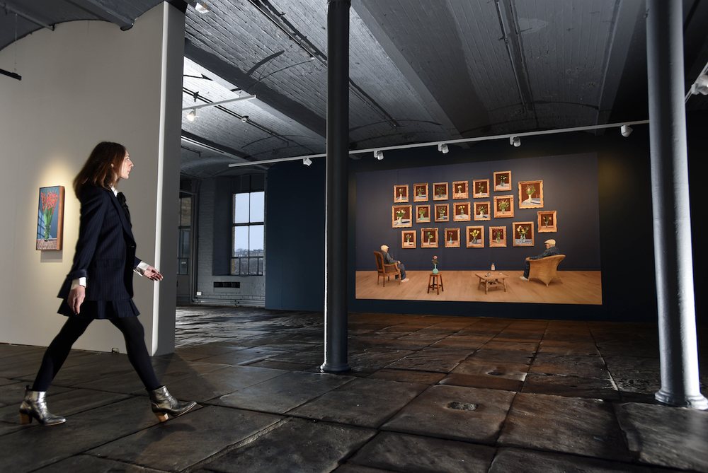 20 Flowers for 2025 and Some Bigger Pictures at Salts Mill: the twenty framed iPad flower paintings on the gallery wall, with a visitor walking past