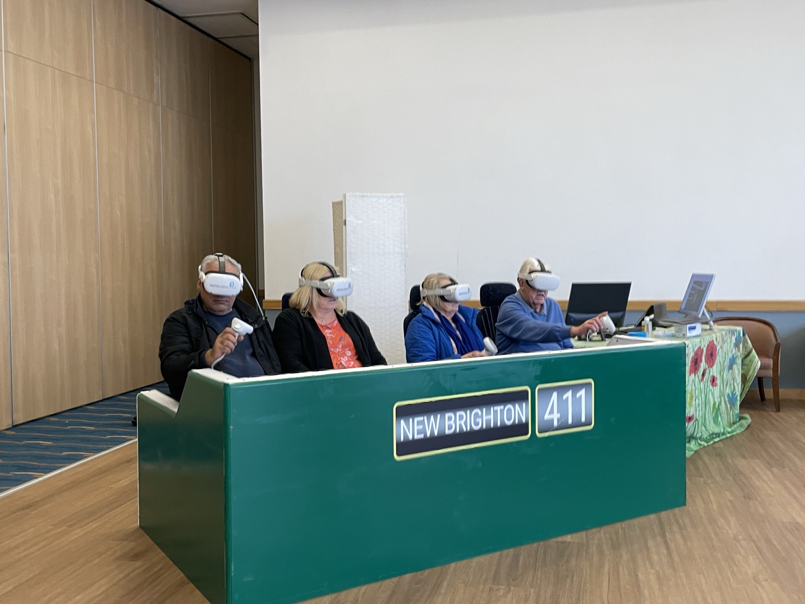 Four visitors in VR headsets riding the open-top bus rig, a green bus front with a New Brighton 411 destination board, at the Wirral consultation event