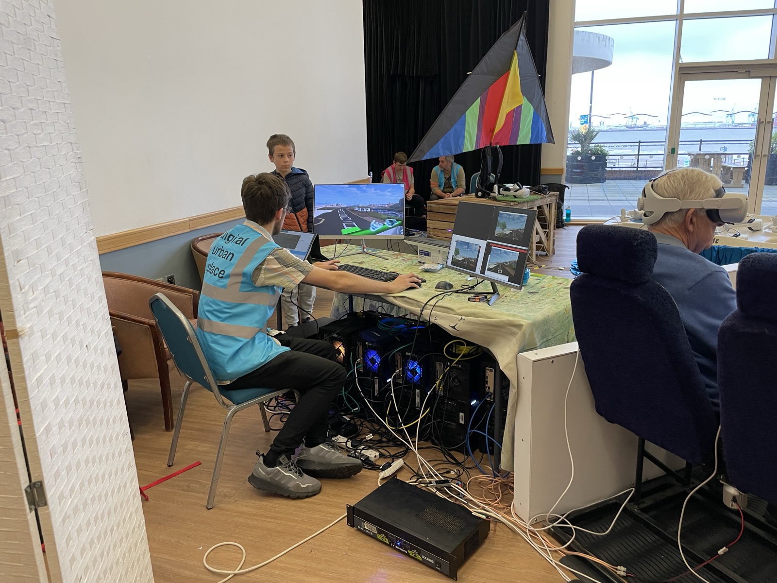 Behind the scenes at the New Brighton event: a crew member at the PCs running the multi-user VR sessions, with screen views of the virtual promenade